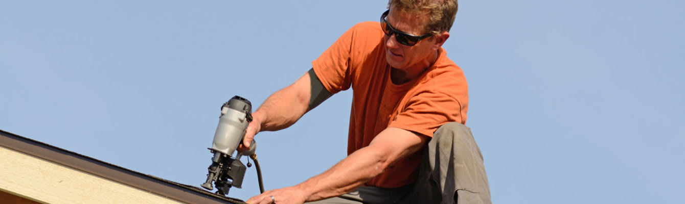 Photo of a homeowner working on top of their roof installing shingles