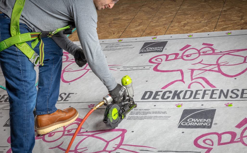 Photo of a contractor walking across a roof with DeckDefense® High Performance Synthetic Roof Underlayment installed