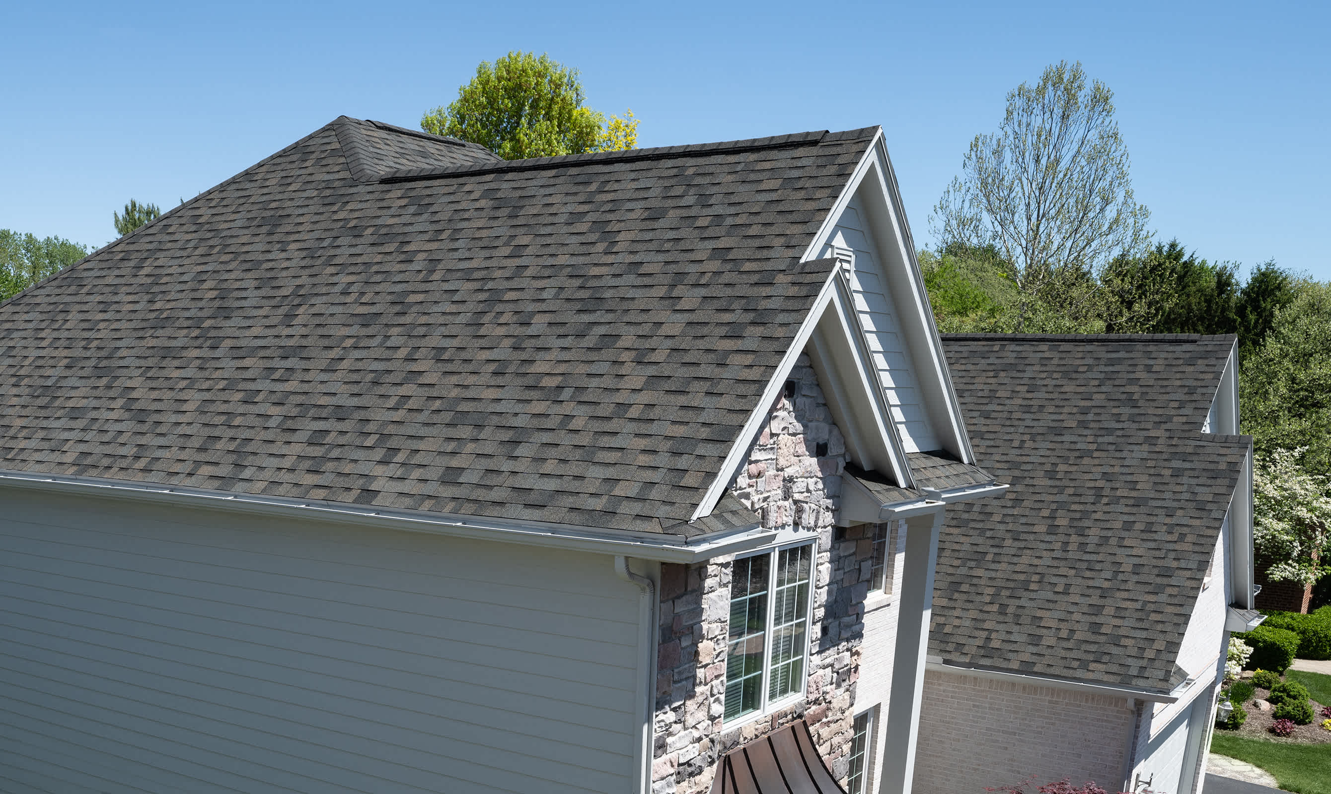 Closeup photo of a brick house with shingles that are a combination of taupe, rich brown and green-gray tones