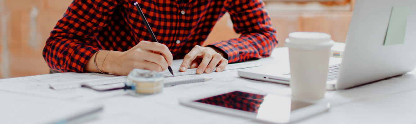 Photo of a person sitting at a desk in front of a laptop taking measurements on a large sheet of paper
