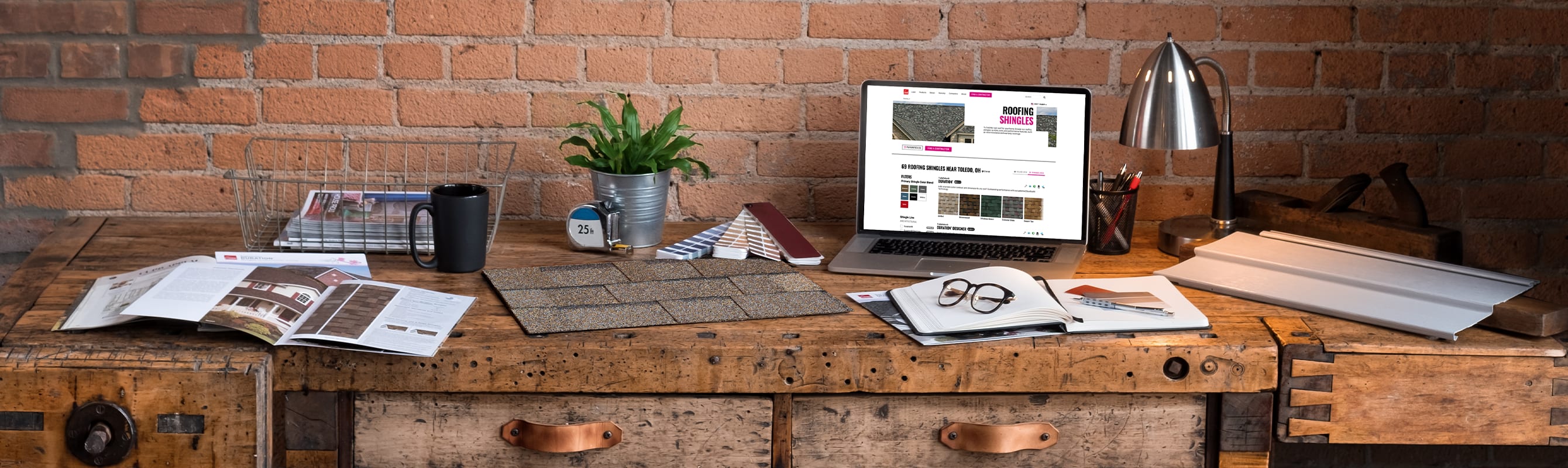 Wood desk with shingle samples, brochures, laptop, and notebook spread out