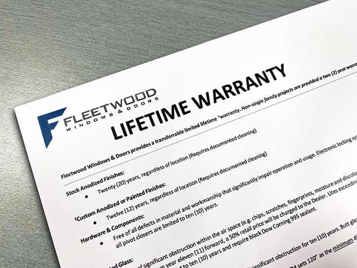Fleetwood Windows & Doors lifetime warranty document detailing coverage for anodized finishes, painted finishes, hardware components, and insulated glass, displayed on a gray textured surface.