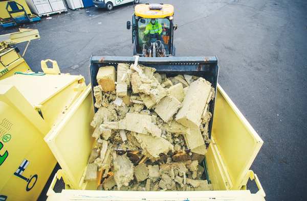 en gravemaskin som dumper brukt steinull i en container