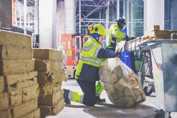 Arbeidere i sikkerhetsutstyr samler steinull for resirkulering