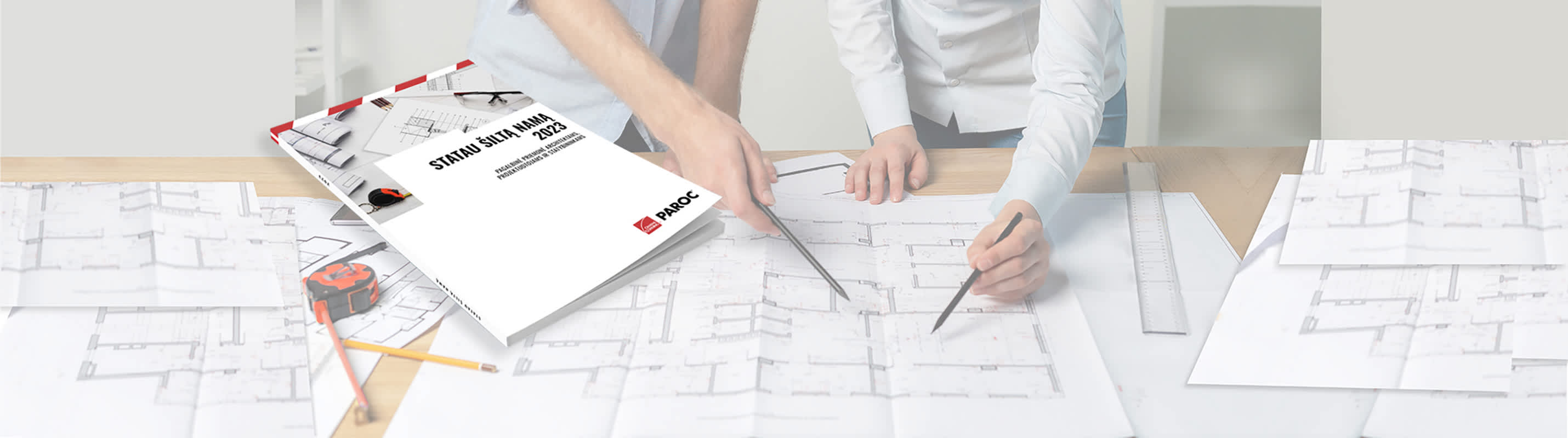 katalogas "statau šiltą namą", gulintis ant stalo kartu su liniuotėmis ir brėžiniais, prie stalo stovi du vyrai ir rodo į brėžinius