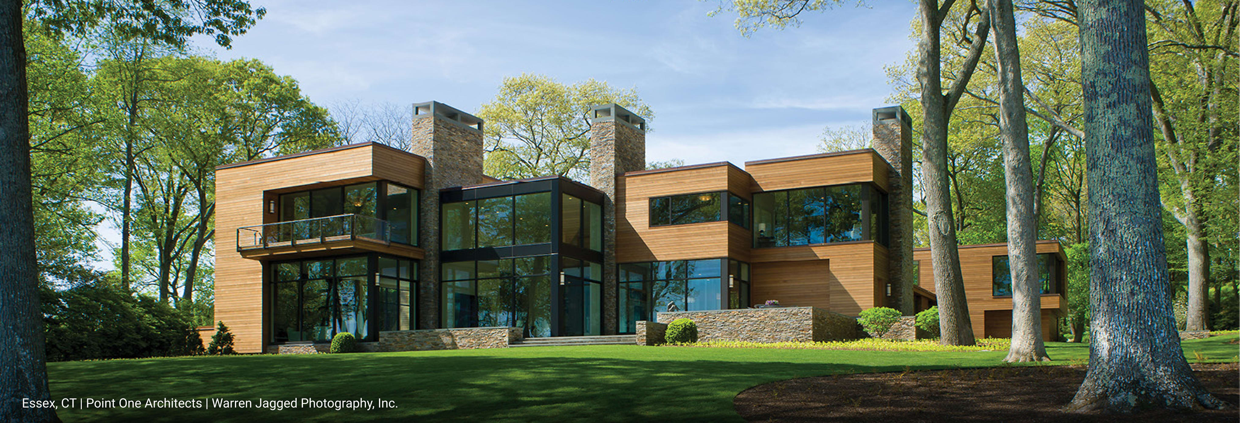 Modern house with horizontal wood panels and many large windows, situated among trees