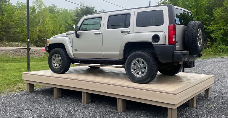 SUV parked on a raised platform made of light-colored decking, demonstrating the structure’s strength.
