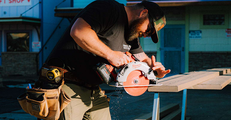 Construction worker using a circular saw to cut a decking board on an outdoor job site.