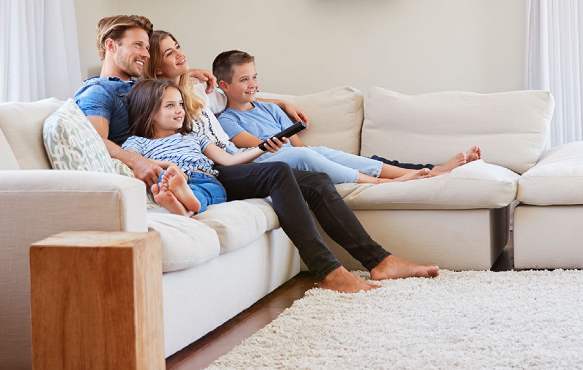 family of two adults and two children lounging on a couch in a living space