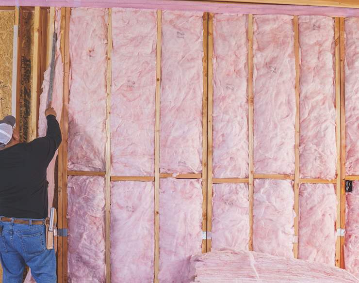 An installer pushed pink insulation batts into wall cavities.
