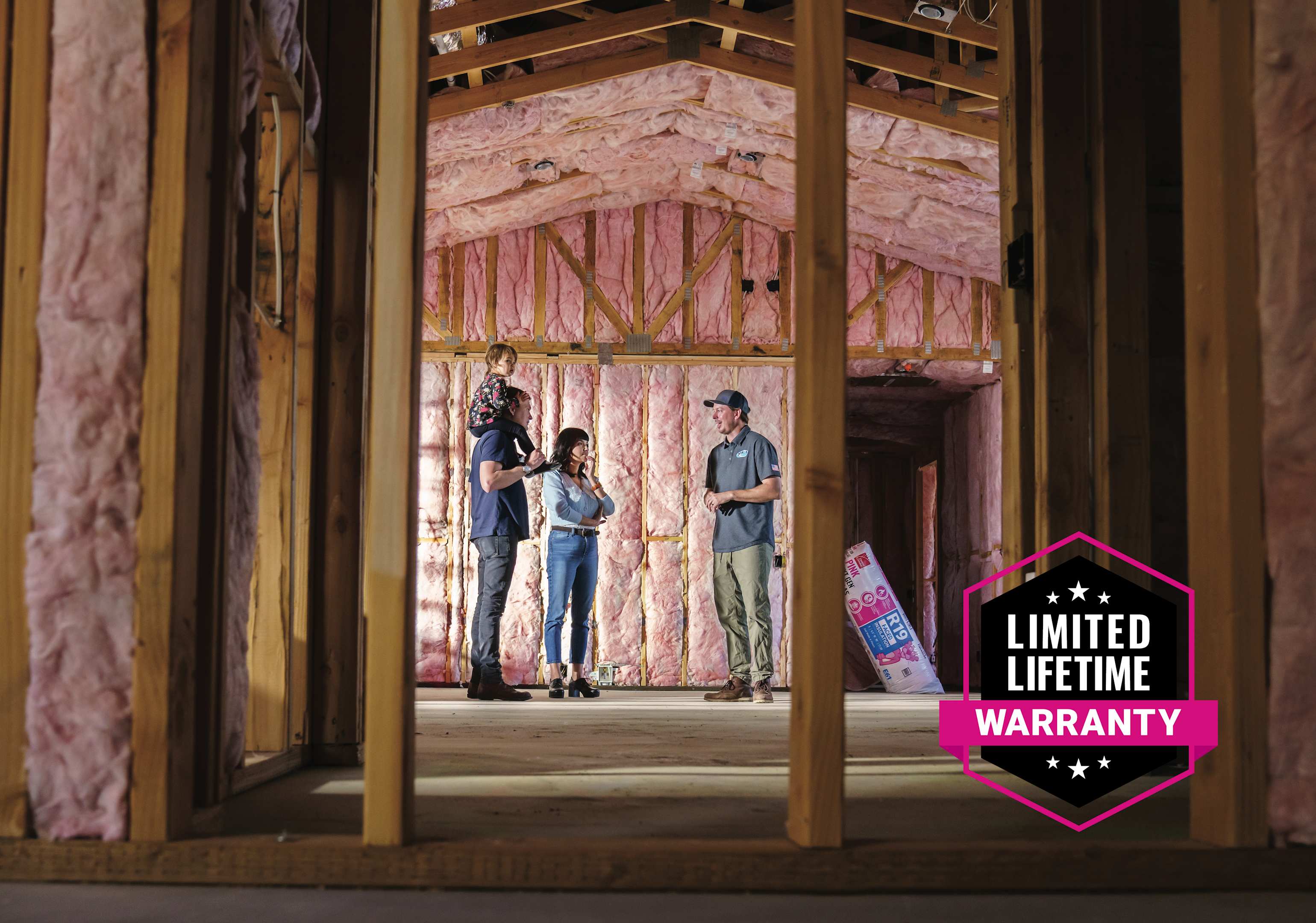 A family walks through their new under construction house with their builder while the open wall cavities have fiberglass installed