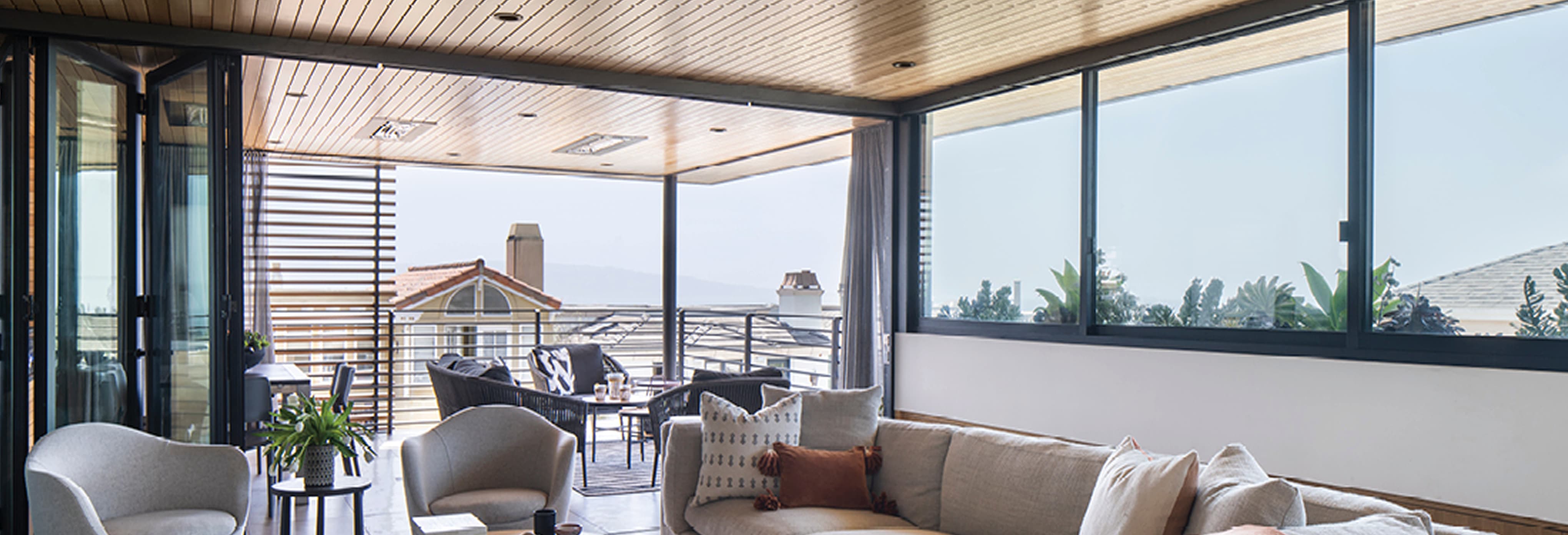 Modern dining area with oval wooden table surrounded by upholstered chairs, minimalist white walls, built-in shelving with decorative accents, and open-concept layout featuring lounge seating and natural wood ceiling.