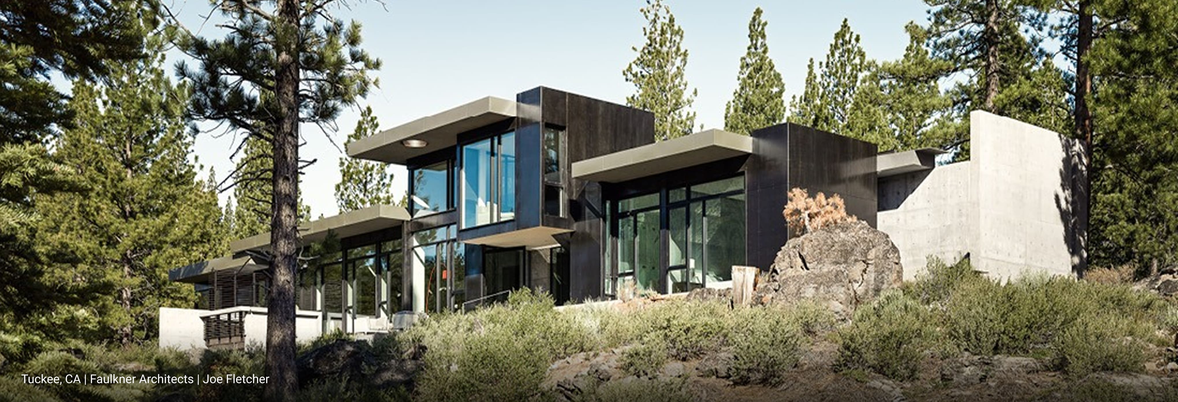 Contemporary mountain home in Truckee, California featuring flat rooflines, dark metal siding, and expansive floor-to-ceiling glass windows, surrounded by pine trees and rugged natural landscape.