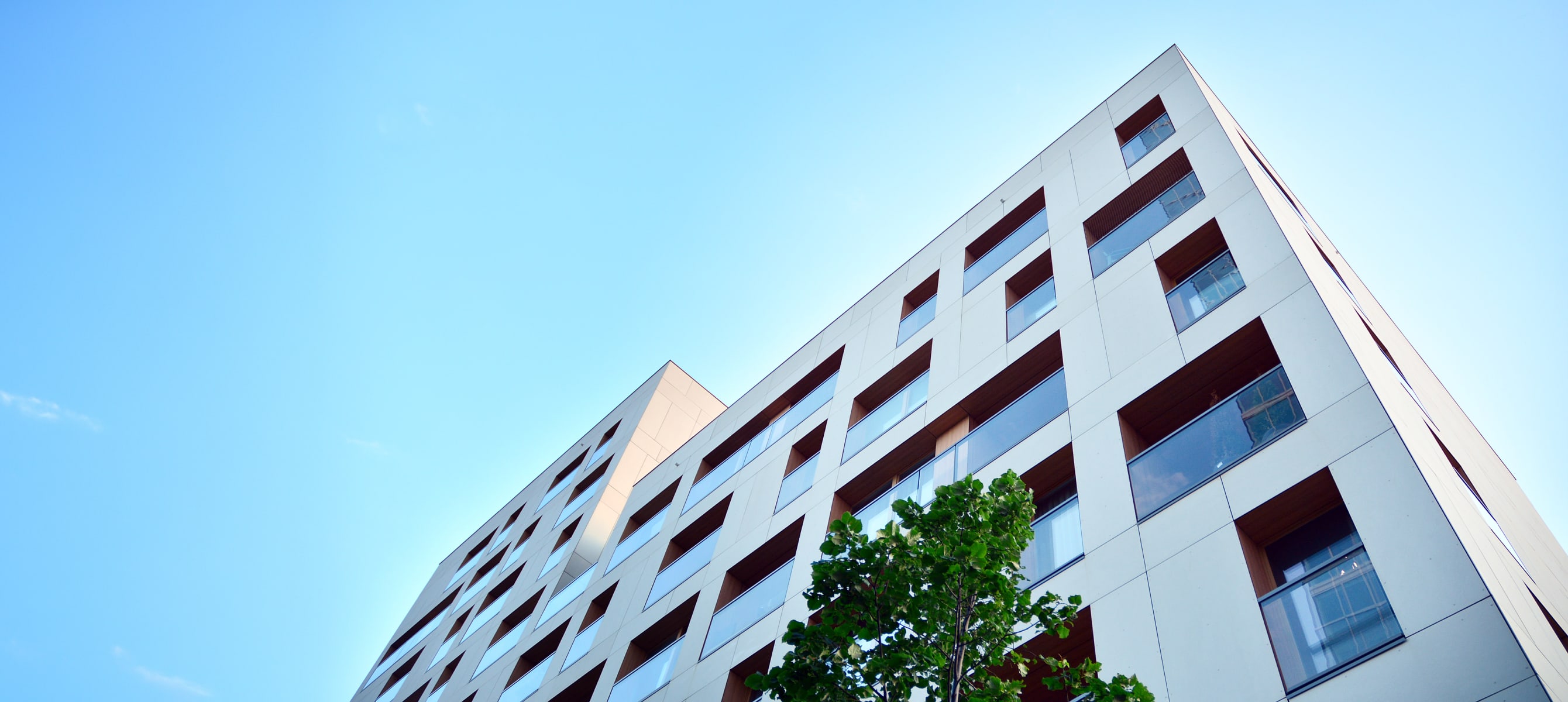 A white building with ventilated facade is seen from beneath with a light blue sky in the background.