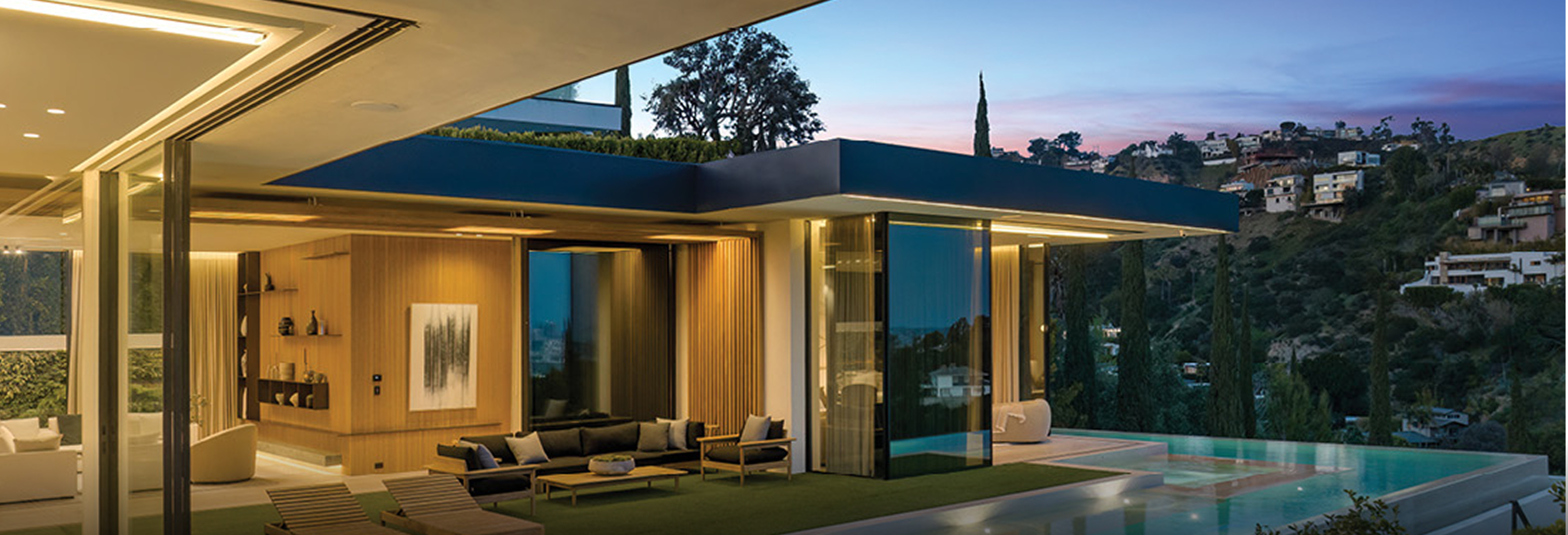 Minimalist modern home entrance with large pivot glass door, black vertical panels, white walls, and wooden ceiling accents overlooking scenic landscape.