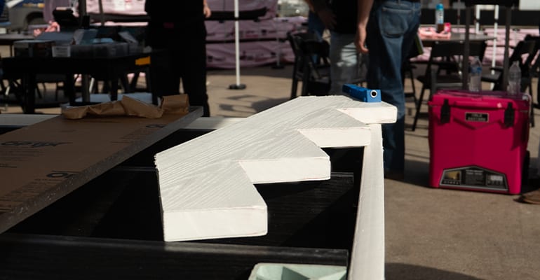 White textured stair stringer piece resting on a workbench at a construction site with tools and materials in the background.