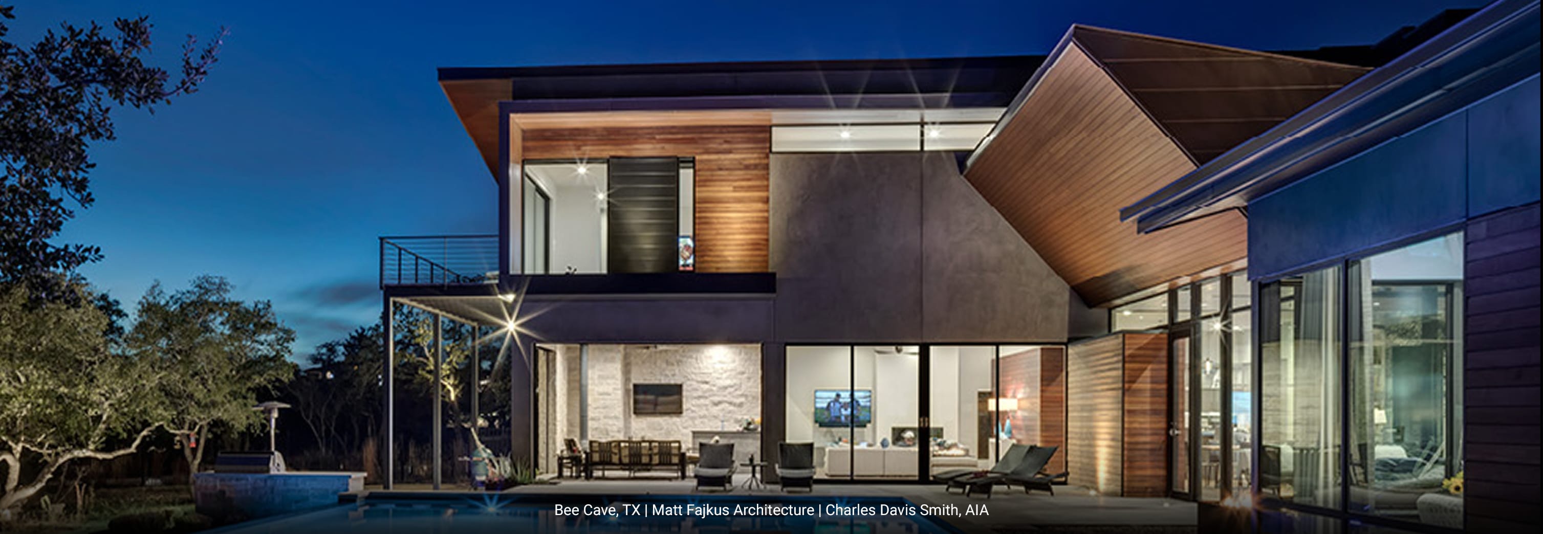 Contemporary luxury home in Bee Cave, Texas featuring angled rooflines, natural wood siding, exposed concrete walls, and expansive floor-to-ceiling glass windows overlooking a modern pool and outdoor lounge area.