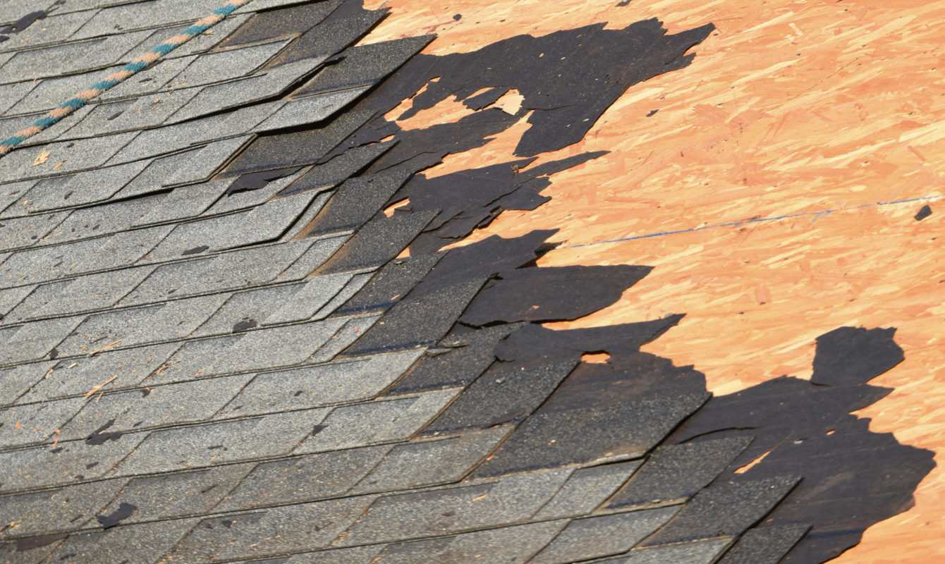Shingles being torn off a roof showing the wood decking underneath.