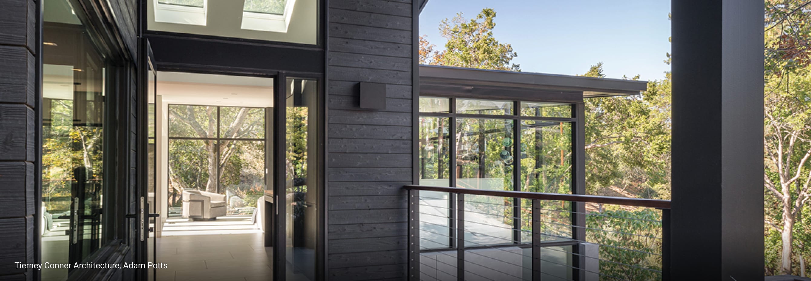 Modern hillside home with dark wood siding, large glass windows, open balcony, and sleek architectural design surrounded by lush greenery.