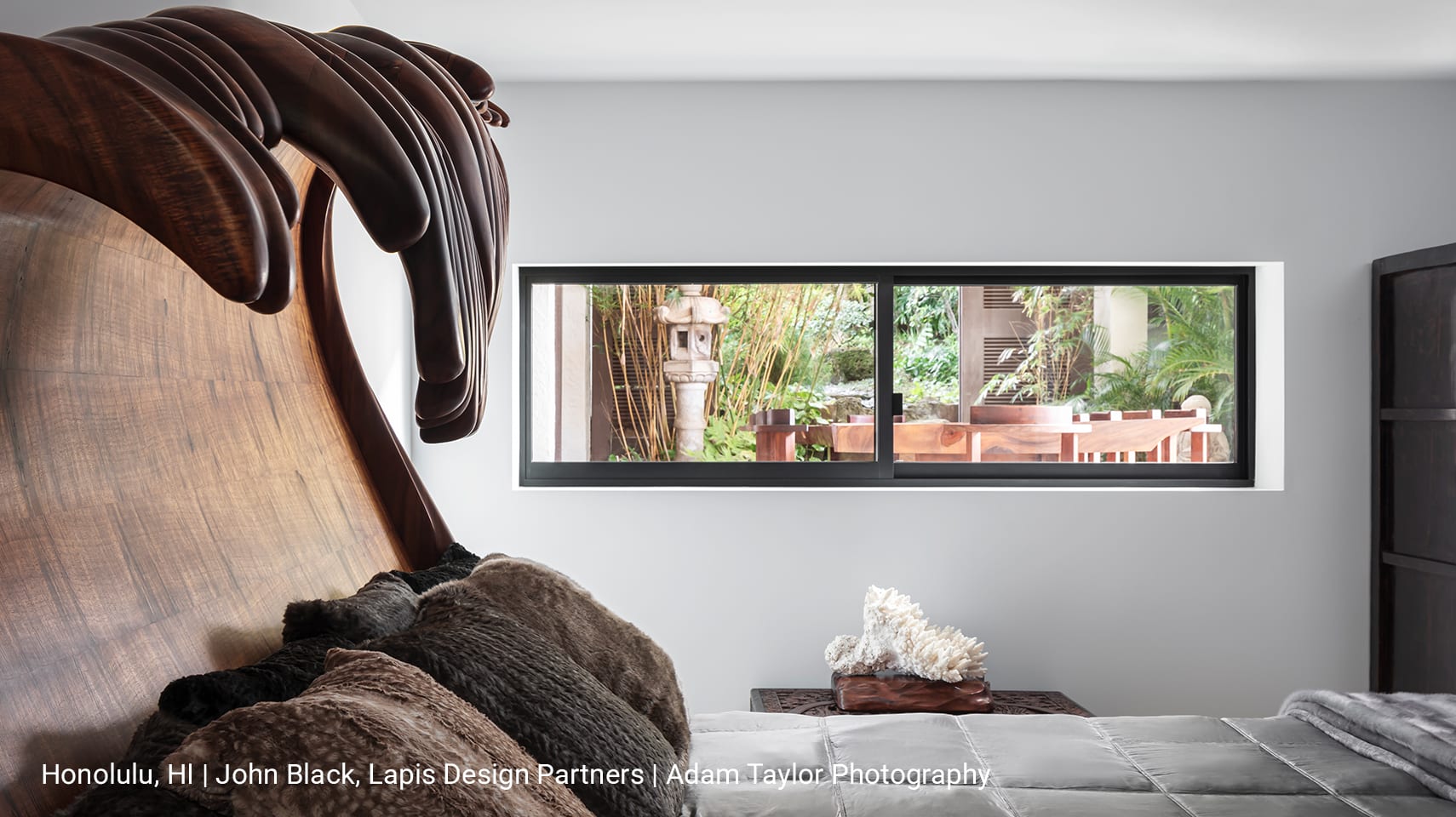 A luxury Hawaiian bedroom with a bed frame shaped like a wave and a sliding Fleetwood 330-T window framing a picturesque backyard.