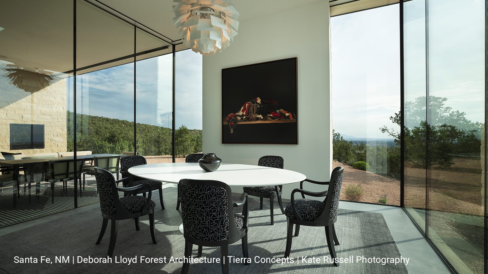 Luxury dining room enclosed by floor-to-ceiling glass walls, featuring a central dining table with expansive views of the Santa Fe wilderness beyond.