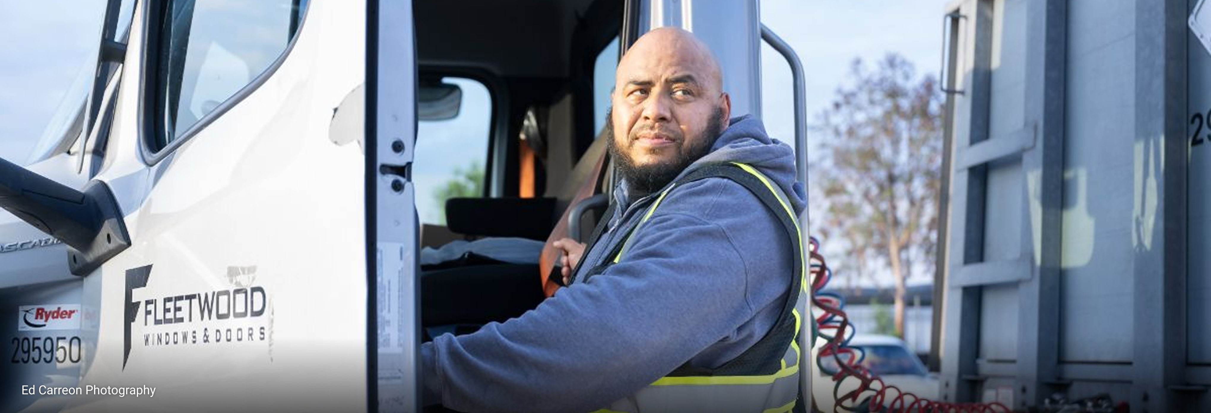 Fleetwood Windows & Doors delivery truck with company logo visible on the door, parked at a loading area with attached trailer and coiled red air hoses.