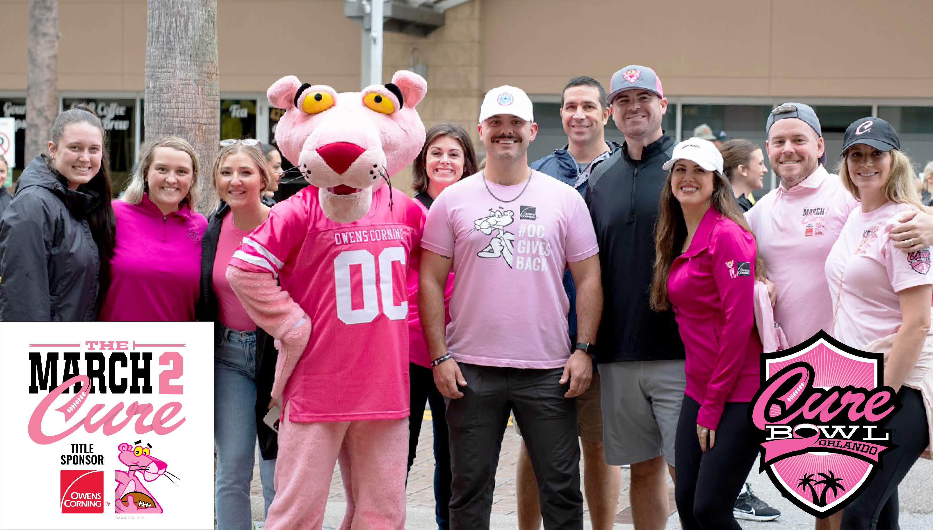 The Pink Panther wearing a pink Owens Corning jersey standing with a group of people wearing a variety of pink shirts.