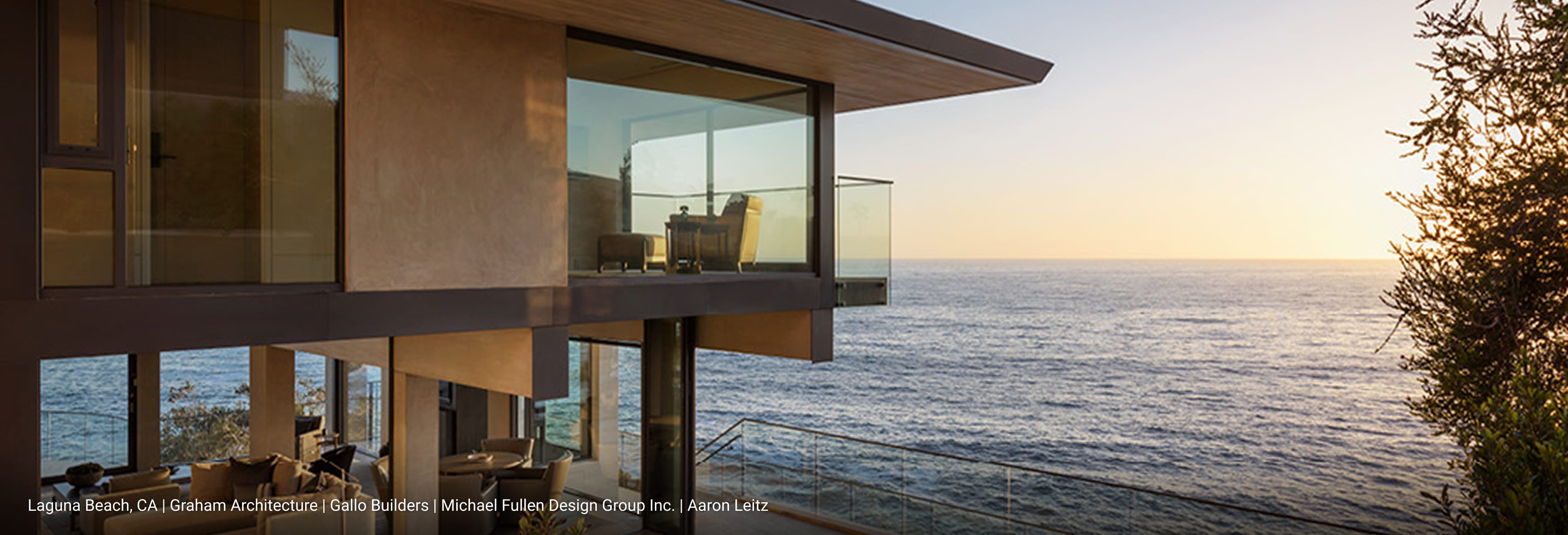 Luxury modern home in Laguna Beach, California featuring cantilevered design, floor-to-ceiling glass walls, wraparound balcony with glass railing, and panoramic ocean views at sunset.