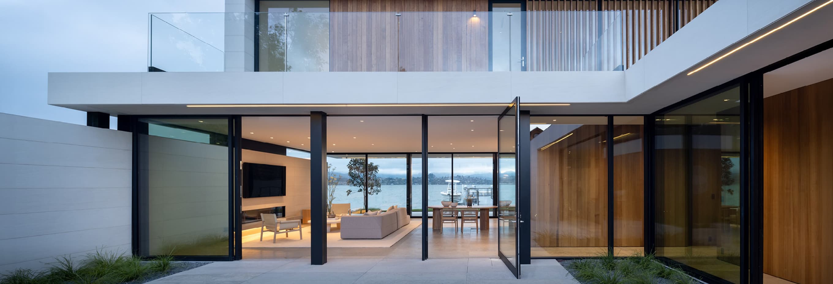 Modern single-story home with clean architectural lines, large glass windows, minimalist landscaping, and warm interior lighting at dusk.