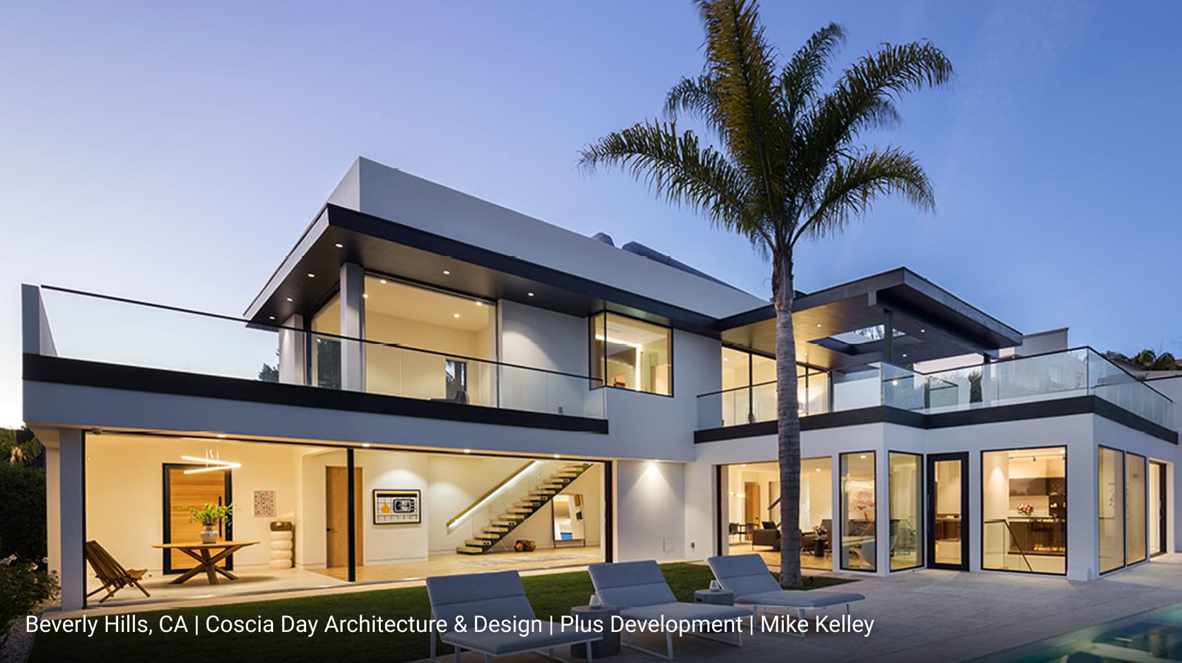 Luxury modern home in Beverly Hills, California featuring flat roof design, white stucco exterior, black trim accents, and expansive glass walls with wraparound balcony, complemented by outdoor lounge area and palm tree landscaping.