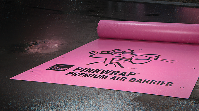 Owens Corning Roofing PinkWrap Premium Air Barrier desenrollada sobre pavimento oscuro y húmedo